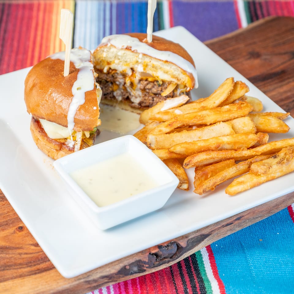 Two saucy sliders with cheese, french fries, and dipping sauce on a white plate over a colorful blanket.